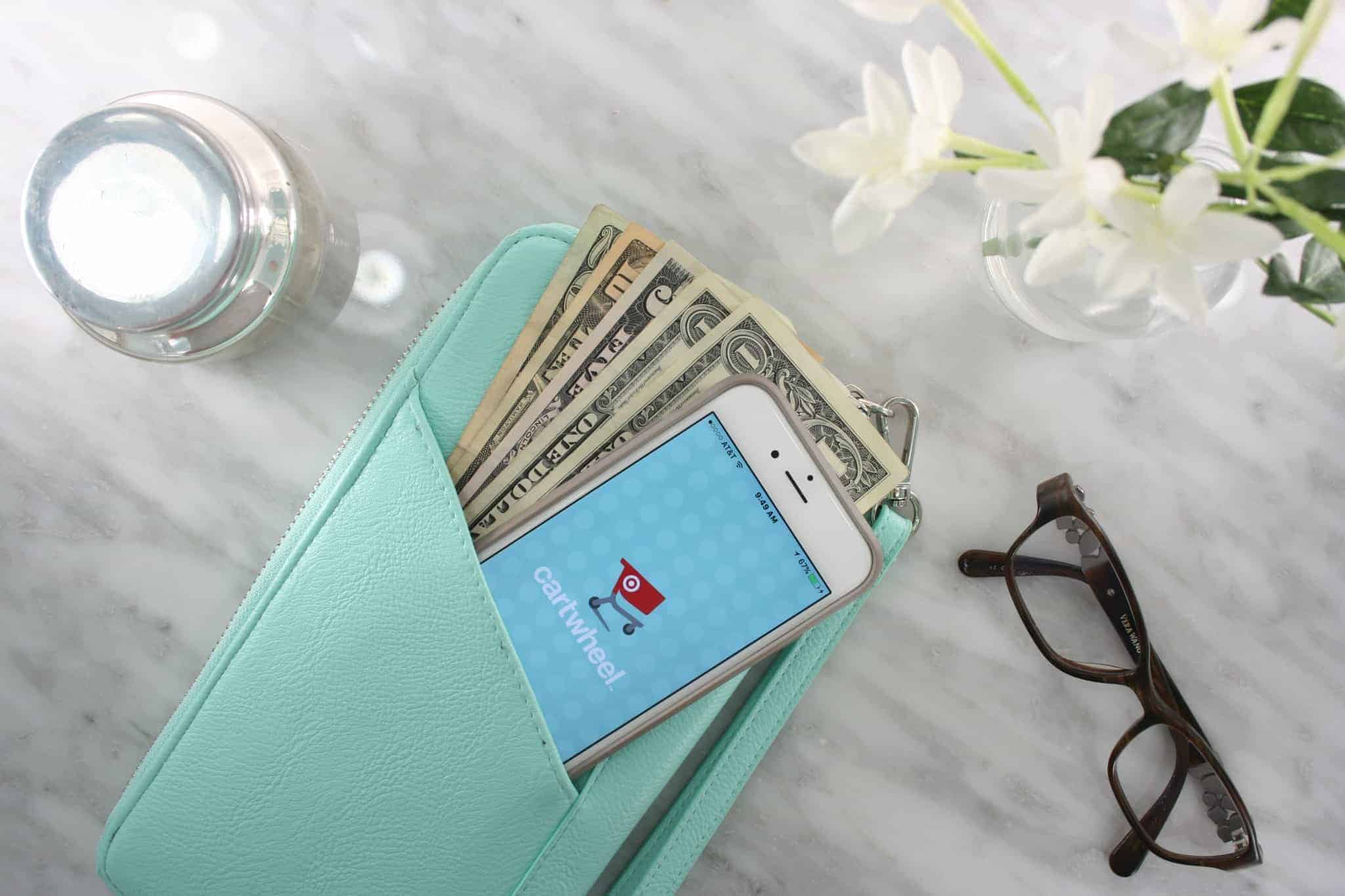a wallet with money and a phone on a table next to glasses and some flowers