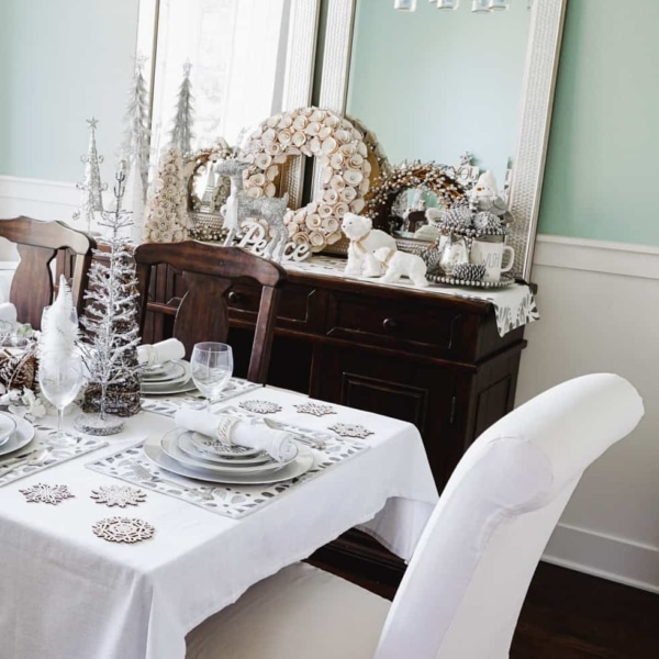 A dining room table and buffet decorated for Christmas with muted silver and white decorative items including decorative trees, woodland creatures, and wreaths. 