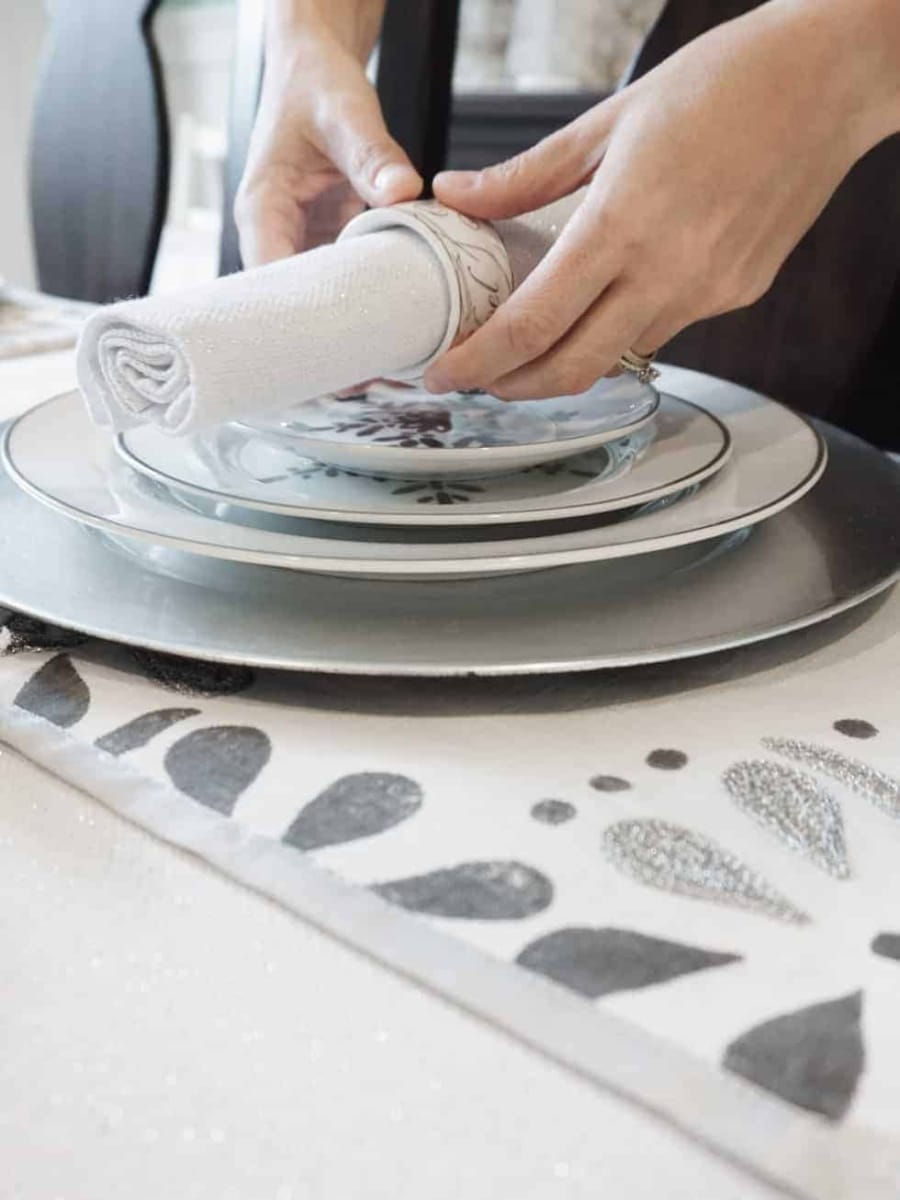 Placing a napkin with Christmas napkin ring on top of a set of silver designed Christmas plates.