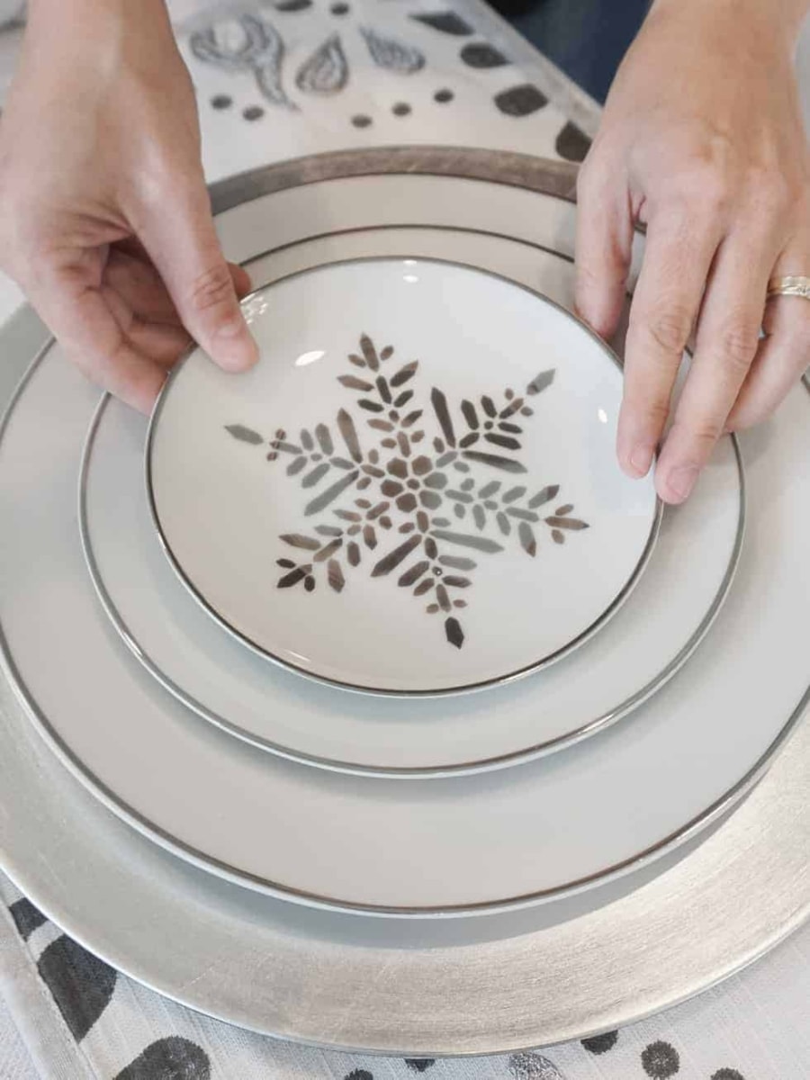 Setting up a dining room table place setting with Christmas plates with a silver snowflake pattern.