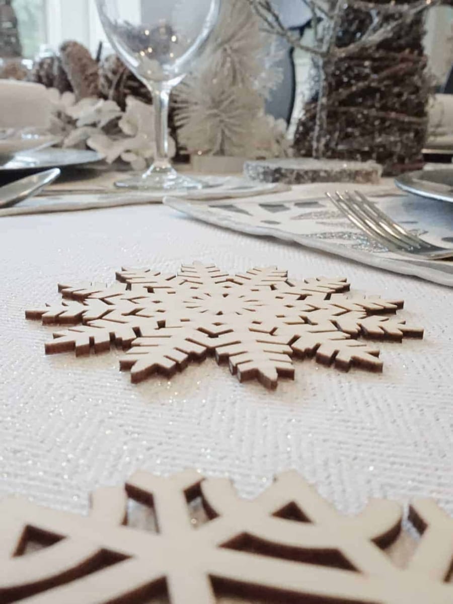 Wood cut out snowflake coasters sitting on a shimmering tablecloth.