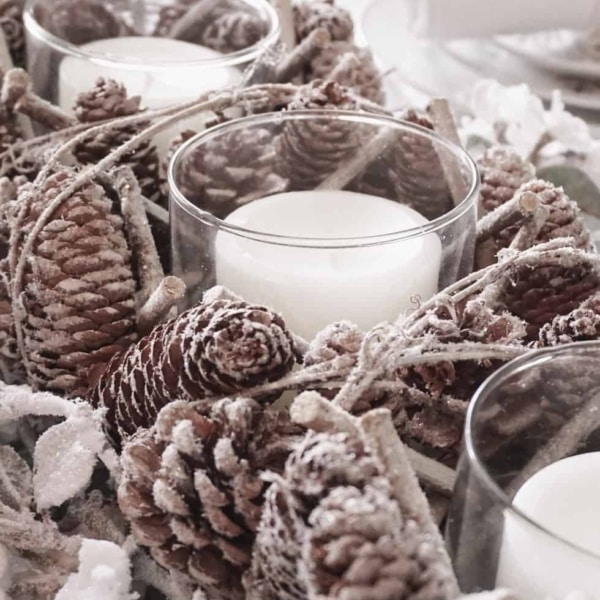 A pine cone table centerpiece with white candles.