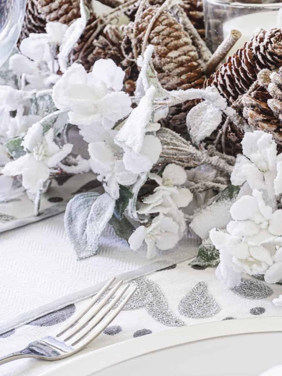 A closeup of the place mat with silver Christmas designs with a table centerpiece in the background surrounded by frosted florals.