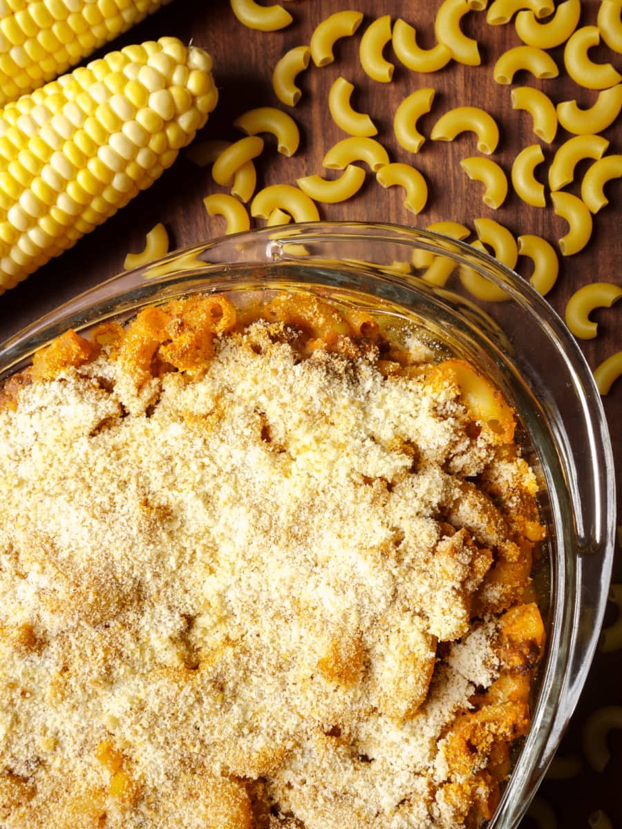 a baking dish with fresh and hot beef casserole on a table with uncooked macaroni pastas and corn