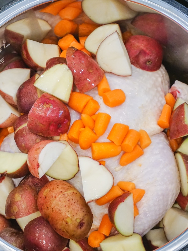 Raw, whole chicken, cut up baby red potatoes, and baby carrots inside Instant Pot ready to be cooked.