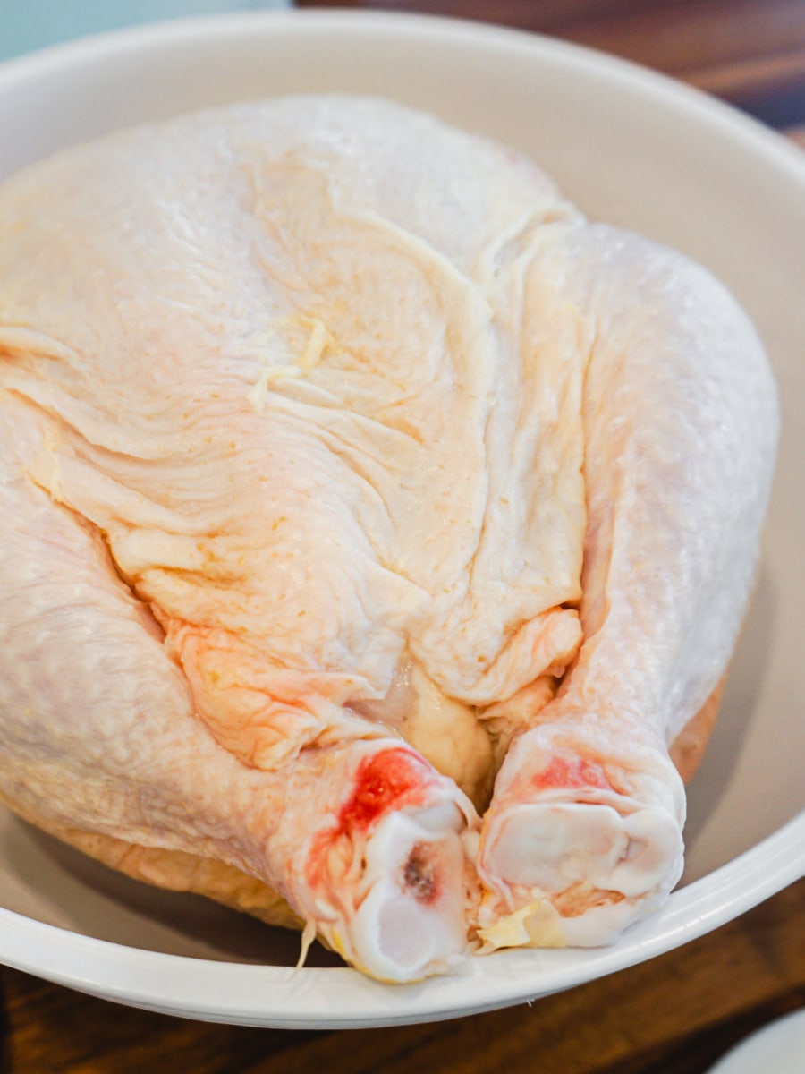 A raw, whole chicken in a large bowl