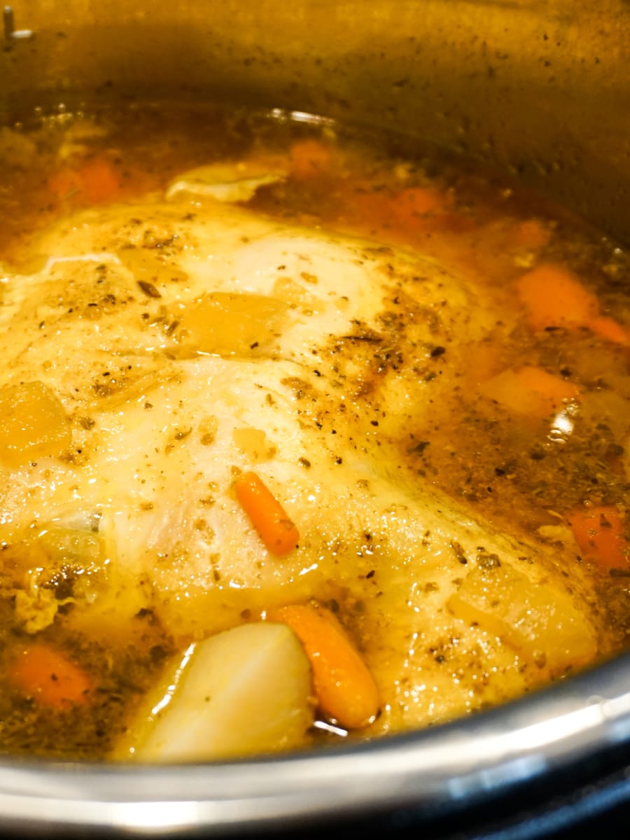 an instant pot with a whole chicken, baby carrots and potatoes.