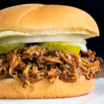 close up of a dr pepper pulled pork sandwich topped with onions and pickles