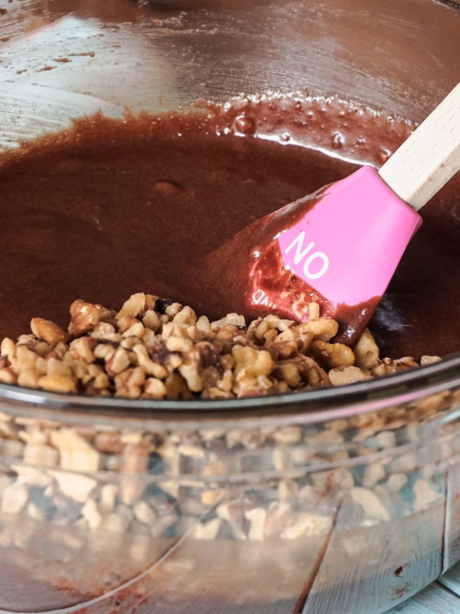 adding nuts to fudgy brownie mixture in mixing bowl