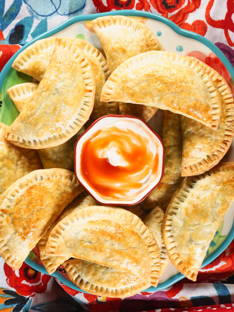 Beef and potato empanadas on a large plate with sour cream and tabasco dip