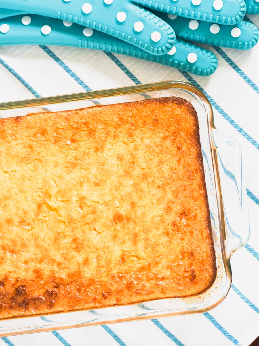 top view of baked creamed corn casserole and two oven gloves