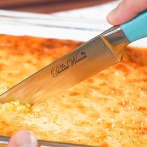 slicing off a piece of corn casserole from a baking dish