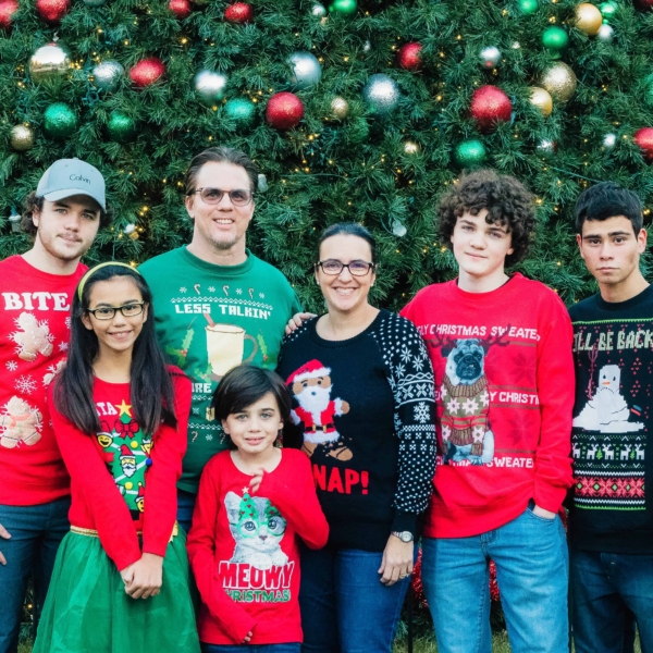 the whole family wearing christmas sweaters in front a christmas tree