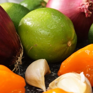 ingredients including lime, purple onion, habanero peppers and garlic are laid out on a cutting board ready for making a habanero salsa