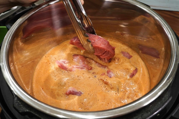 pork shoulder strips being added to the instant pot to make cochinitas pibil