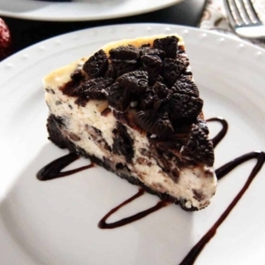 a plate with a slice of chocolate swirl oreo cheesecake topped with oreo bits