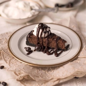 a small slice of chocolate espresso cheesecake topped with whipped cream and chocolate drizzle