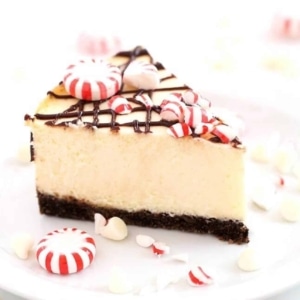 a slice of white chocolate peppermint cheesecake topped with peppermint pieces and chocolate drizzle