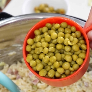 adding peas to a macaroni salad made with spam and peas