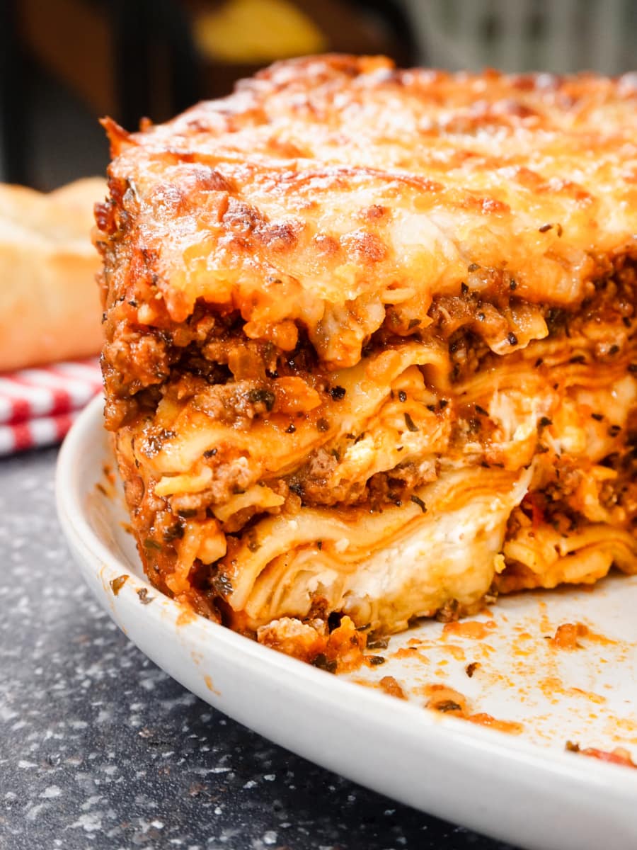 side view of a large lasagna sitting on a serving plate with slices taken out of it exposing its layers of meat, cheese, and pasta