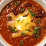 top view of a bowl of texas chili topped with cheese and garnished with green onion