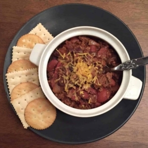 a plate with a bowl of chili with canned beans and crackers