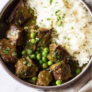 a bowl of beef stew with peas and rice garnished lightly with cilantro