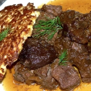 a large plate with beef stew garnished with dill