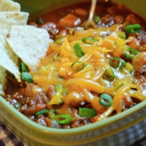 chili with dried beans in a bowl topped with cheese, green onion, and chips