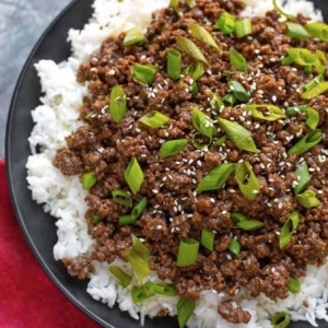 a plate of korean ground beef garnished with sesame seeds and scallions on a bed of rice