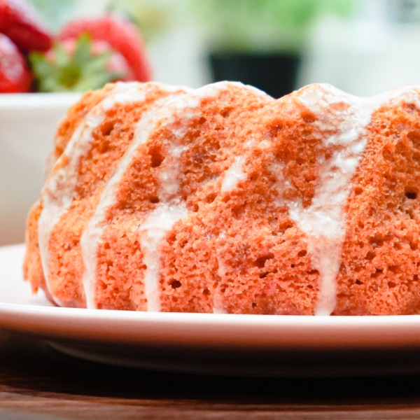 a strawberry and cream cake on a plate near a bowl of fresh strawberries