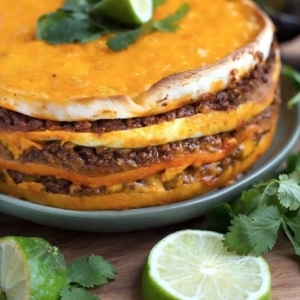 a large taco pie on a plate topped with a lime and cilantro