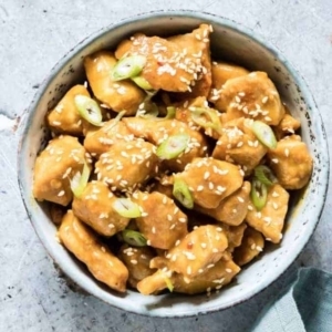 a bowl of orange chicken garnished with sesame seeds and green onion