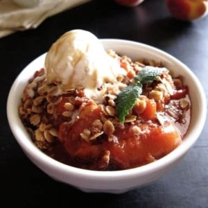 a bowl of peach crisp with a scoop of ice cream on top