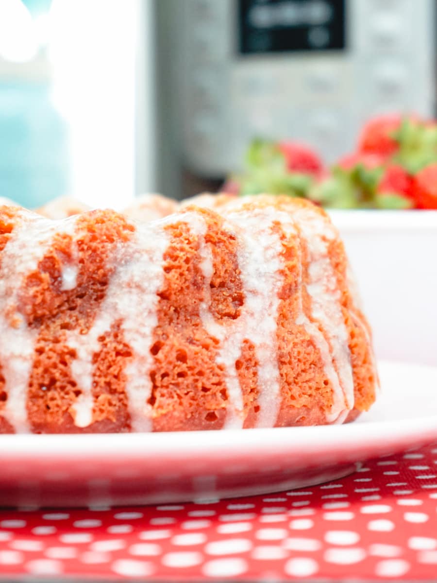 a strawberry and cream cake on a plate with a bowl of strawberries and an instant pot in the background