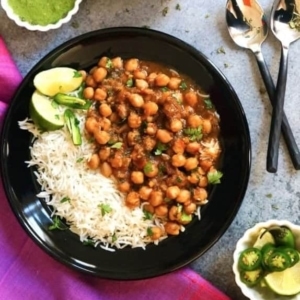 a bowl of punjabi chole garnished with cilantro and two slices of lime