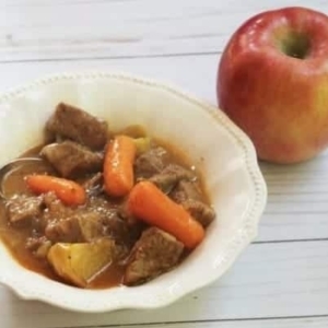 a small serving of beef stew in a bowl next to an apple