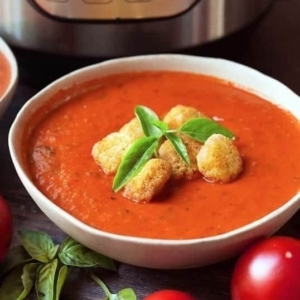 a bowl of fresh tomato basil soup topped with croutons and basil