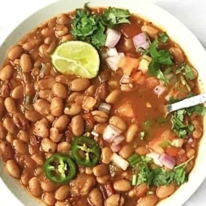 overhead shot of a bowl of mexican pinto beans topped with jalapanos, a slice of lime, and a bed of cilantro