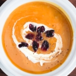 a bowl of instant pot butternut squash soup topped with cream and dried cranberries