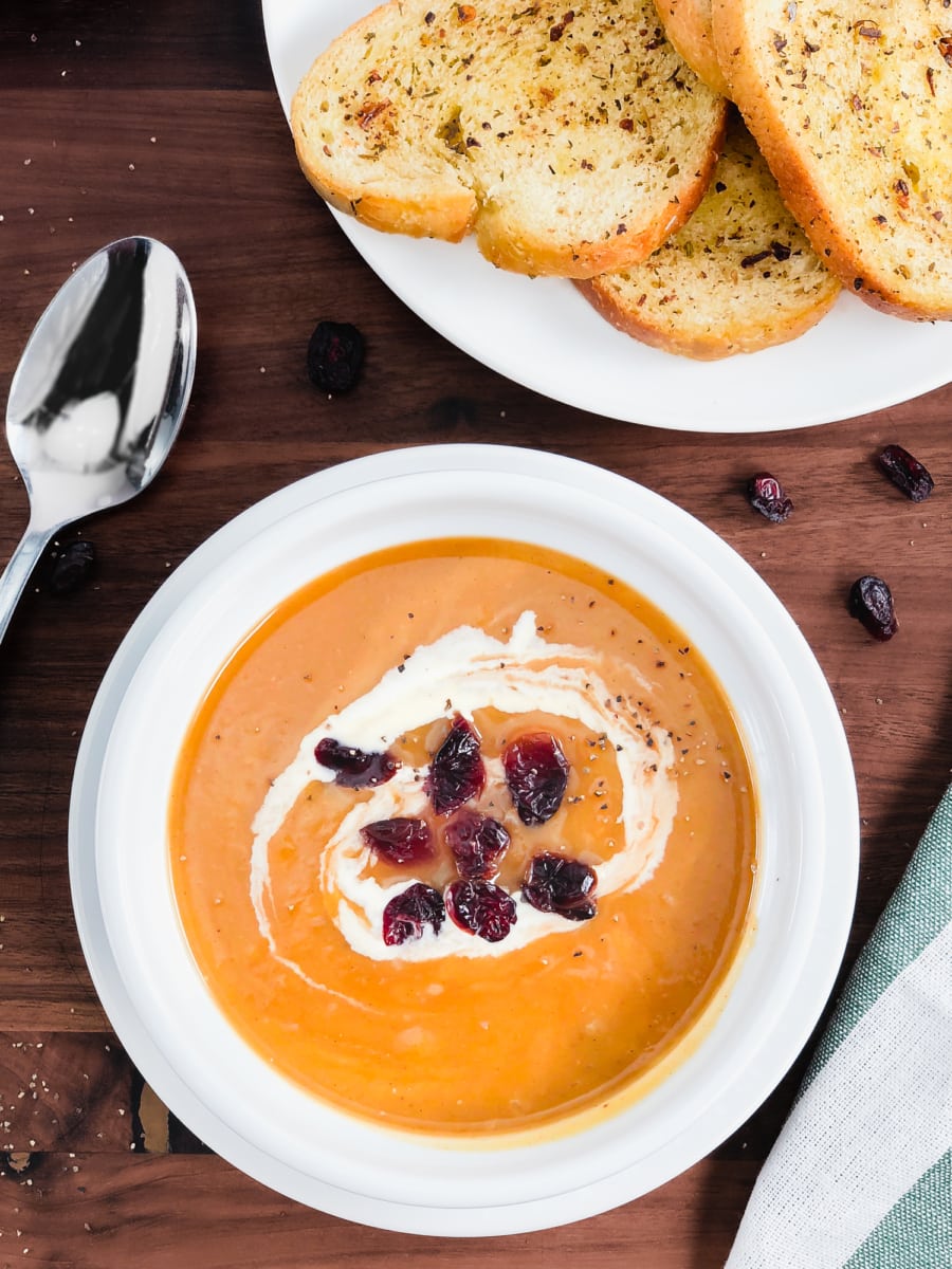 a small bowl of instant pot butternut squash soup topped with cream and dried cranberries