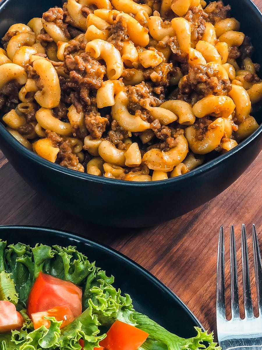 a bowl of cheeseburger mac with a plate of lettuce and tomato