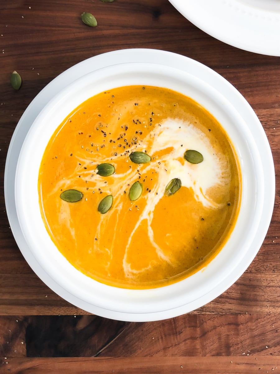 overhead shot of a small bowl of pumpkin soup with cream and pumpkin seeds