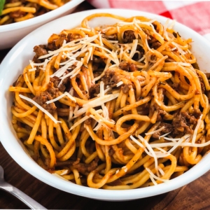 spaghetti and meat sauce served in a bowl topped with shredded parmesan