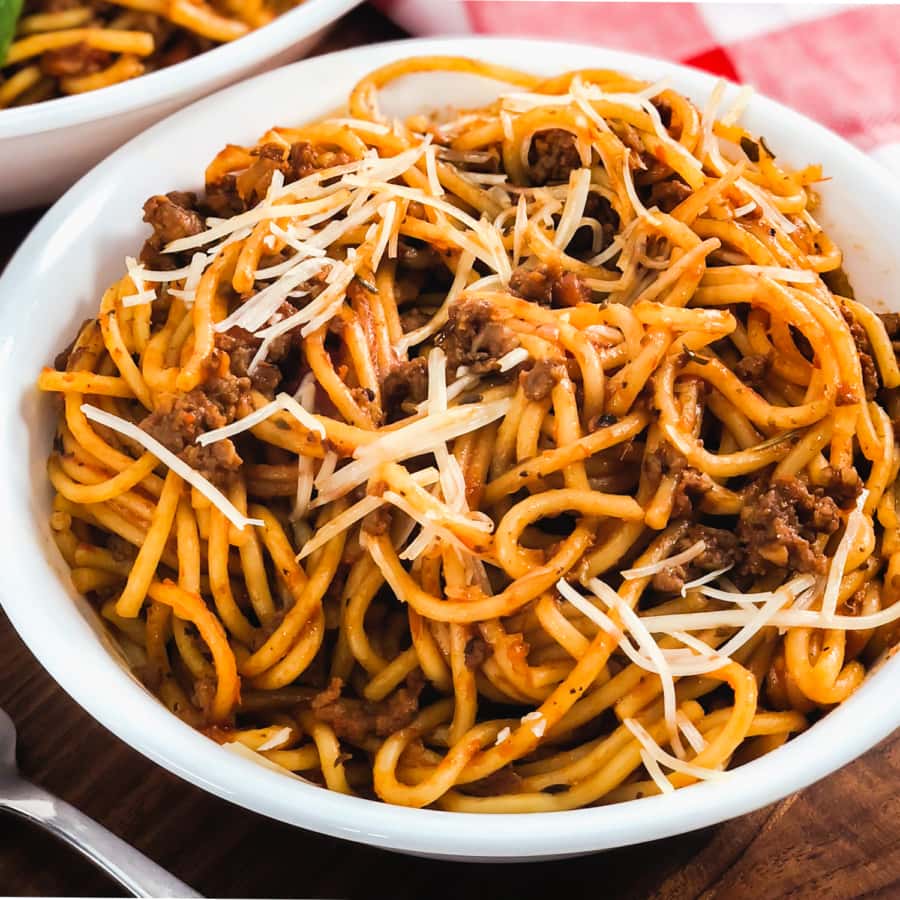 spaghetti and meat sauce served in a bowl topped with shredded parmesan 