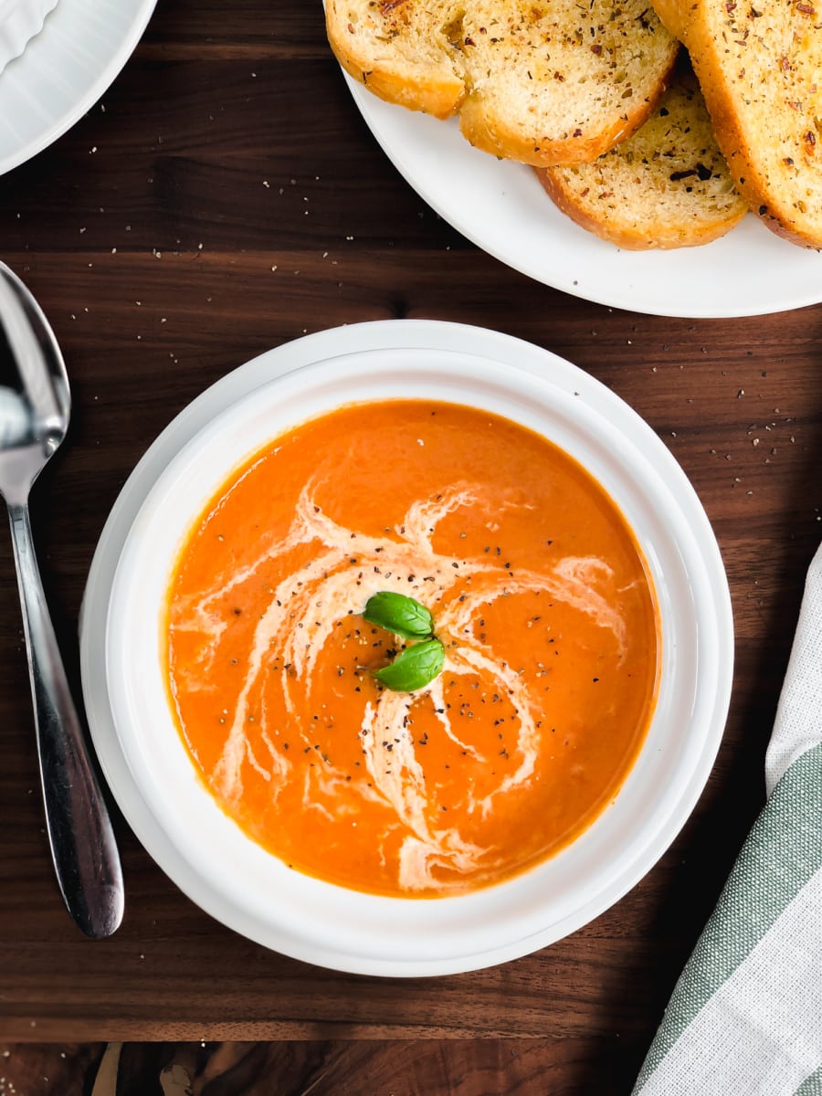 a served bowl of tomato soup garnished with basil leaves