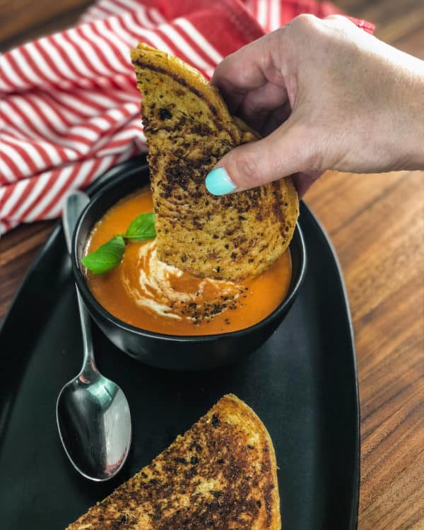 dipping a grilled cheese in a bowl of instant pot tomato soup