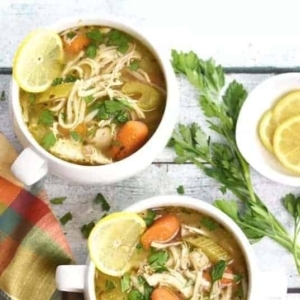 overhead shot of chicken noodle soup in a bowl garnished with cilantro and a think lemon slice