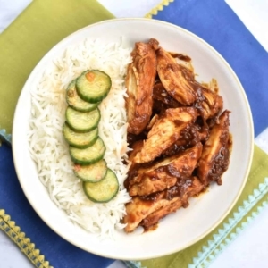 overhead shot of korean spice chicken on a plate with rice and cucumber slices