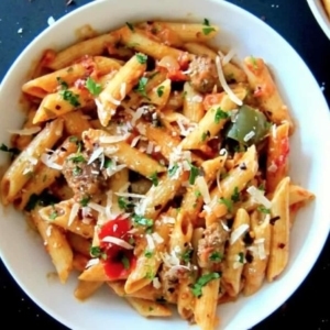 overhead shot of creamy tomato and sausage pasta with cilantro and shredded cheese